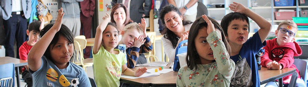 students in a classroom with raised hands and smiling faces